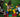 Three children sitting on grass, collaboratively arranging jumbo red, yellow, green, and blue blocks into a large square frame.