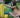 A girl building with colorful blocks on the grass, focused on stacking a yellow block. 