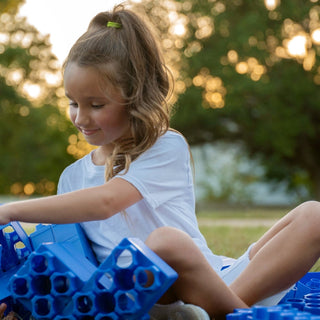 A young girl playing with jumbo building blocks in the backyard.
