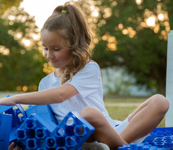 A young girl playing with jumbo building blocks in the backyard.