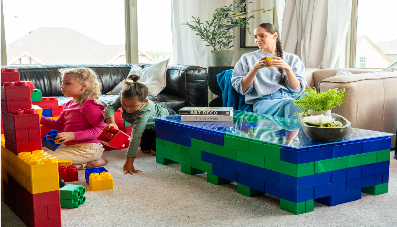 Three young children sitting on the floor, engaging in creative play with colorful building blocks in a cozy living room setting.