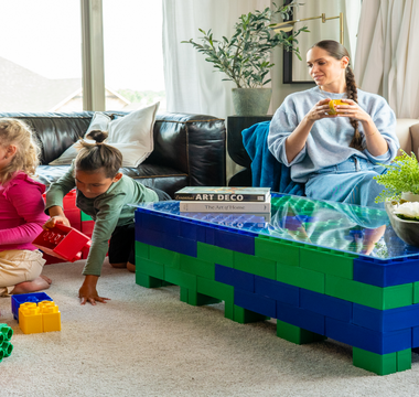 Three young children sitting on the floor, engaging in creative play with colorful building blocks in a cozy living room setting.