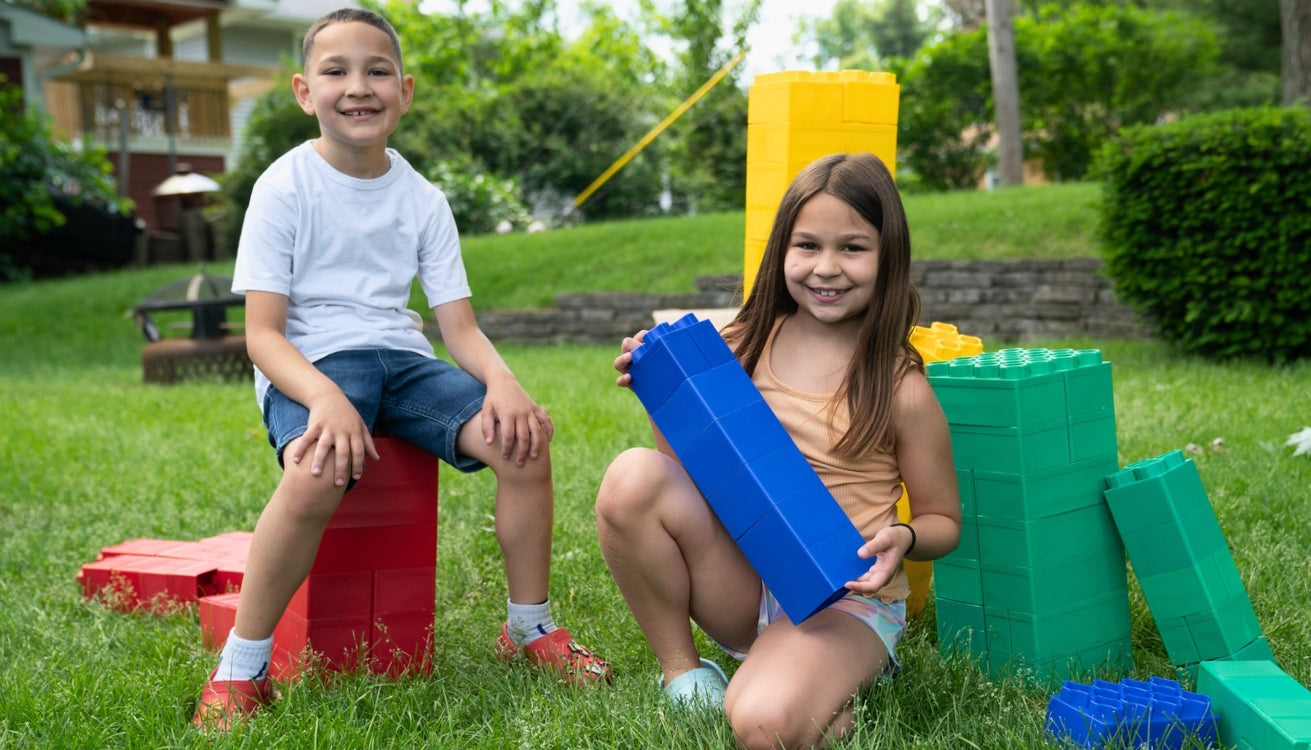 Two children playing happily outdoors with large building blocks, showcasing creativity and teamwork in a fun, playful setting.