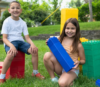 Two children playing happily outdoors with large building blocks, showcasing creativity and teamwork in a fun, playful setting.