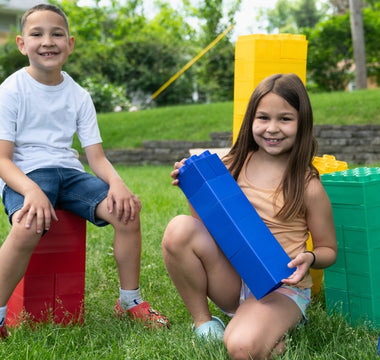 Two children playing happily outdoors with large building blocks, showcasing creativity and teamwork in a fun, playful setting.