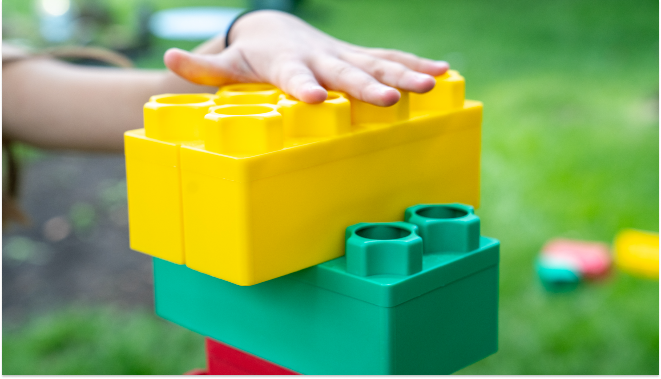 Children constructing a vibrant structure with large building blocks on a grassy lawn, highlighting the fun and educational value of building blocks in outdoor play.