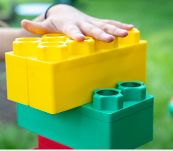 Children constructing a vibrant structure with large building blocks on a grassy lawn, highlighting the fun and educational value of building blocks in outdoor play.