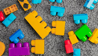Bright and colorful building blocks scattered on a grey carpet, showcasing their vibrant colors and simple design.