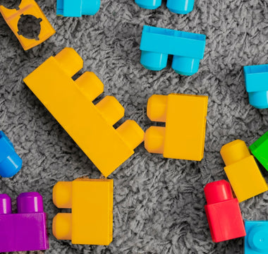 Bright and colorful building blocks scattered on a grey carpet, showcasing their vibrant colors and simple design.