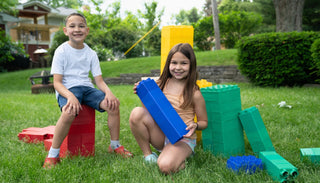 Two smiling children playing with colorful Biggo Blocks in the backyard, demonstrating the fun and creativity these blocks can bring to grandchildren.