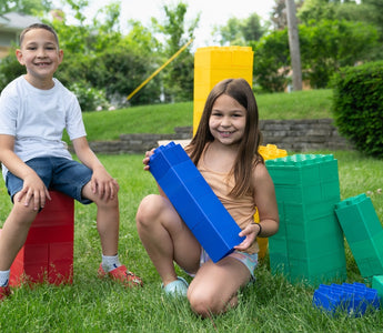 Two smiling children playing with colorful Biggo Blocks in the backyard, demonstrating the fun and creativity these blocks can bring to grandchildren.