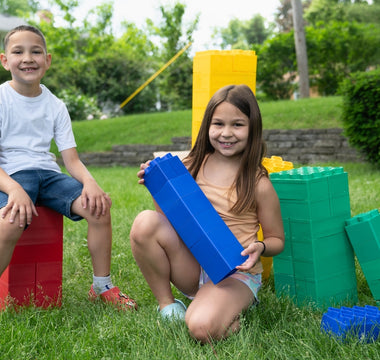 Two smiling children playing with colorful Biggo Blocks in the backyard, demonstrating the fun and creativity these blocks can bring to grandchildren.