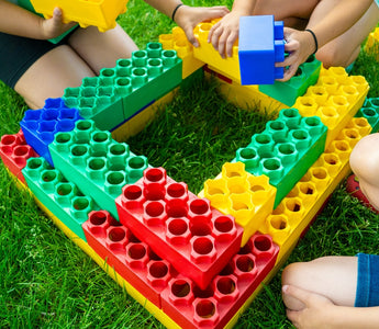 Children constructing a vibrant structure with large building blocks on a grassy lawn, highlighting the fun and educational value of building blocks in outdoor play.