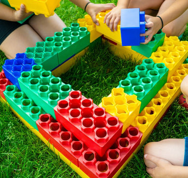 Children constructing a vibrant structure with large building blocks on a grassy lawn, highlighting the fun and educational value of building blocks in outdoor play.