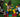 Three children sitting on grass, collaboratively arranging jumbo red, yellow, green, and blue blocks into a large square frame.