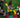 Three children sitting on grass, collaboratively arranging jumbo red, yellow, green, and blue blocks into a large square frame.
