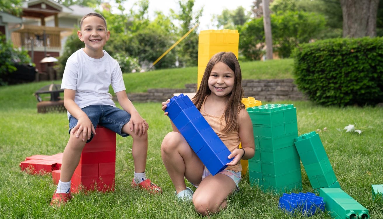 A boy and a girl happily enjoying playing outdoors with colorful jumbo building blocks from Biggo Blocks