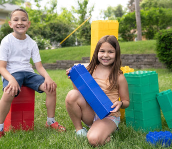 A boy and a girl happily enjoying playing outdoors with colorful jumbo building blocks from Biggo Blocks