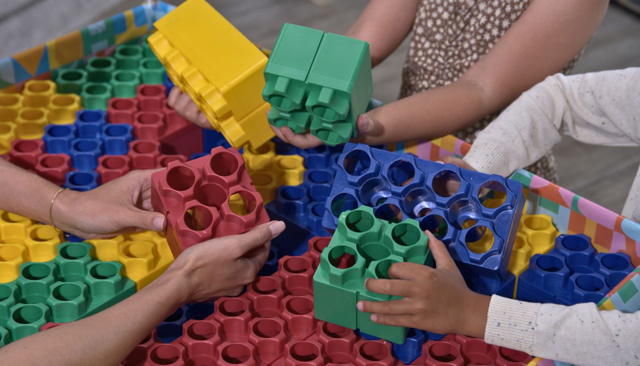 Close-up of hands storing colorful building blocks after a group play session.